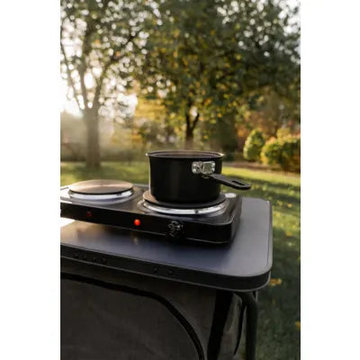 Mestic MKT-120 electric cooker with pot on a camping table as the sun sets behind