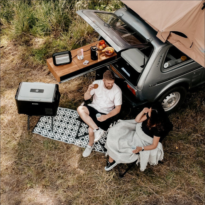 Mestic cool box on its stand at a campsite with people relaxing in camping chairs