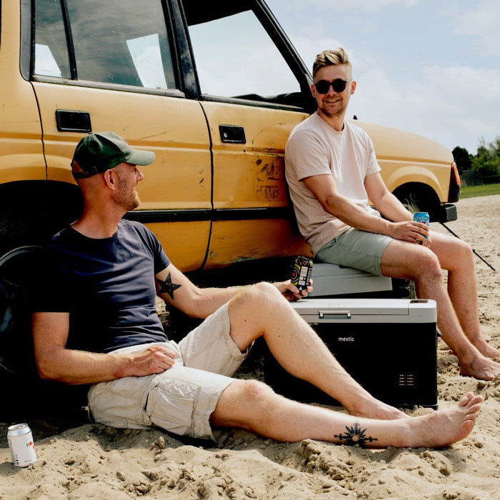 Two friends on the beach with cold drinks and a Mestic cool box on the sand