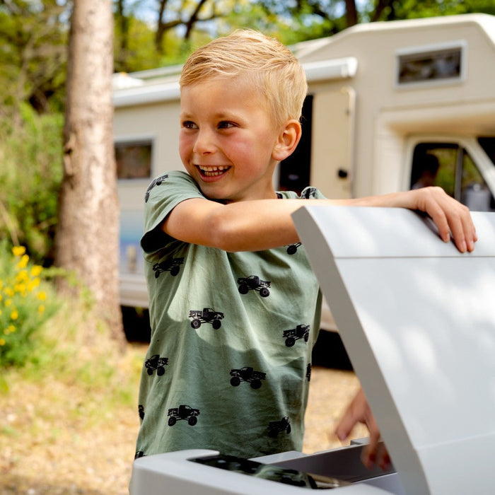 Child smiling while opening a compact Mestic cool box on a sunny family camping trip