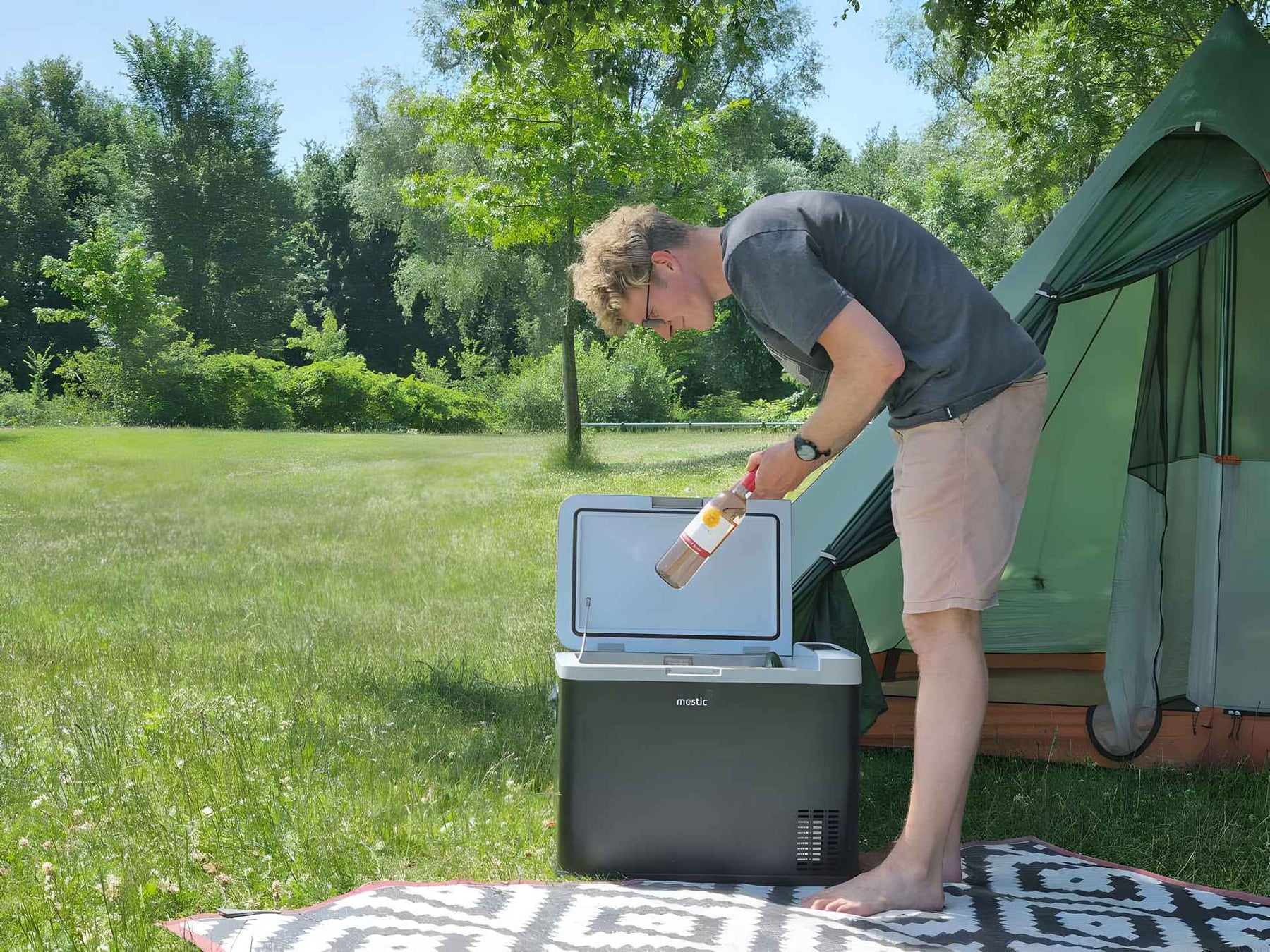 Man placing a wine bottle into a Mestic MCC-35 cool box at an outdoor camping setup
