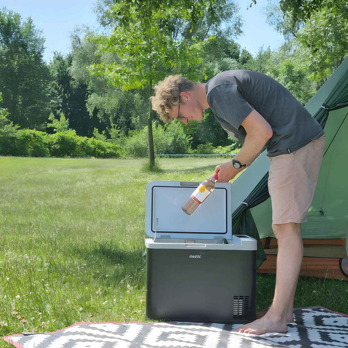 Mestic cool box in use at a campsite on a rug next to a tent — cold drinks and food sorted